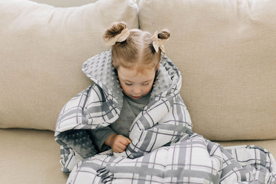 little girl wrapped in gray and white plaid children's blanket