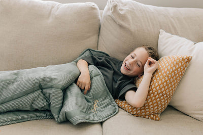 Little boy cuddling on couch with a green dotted stripe children's blanket