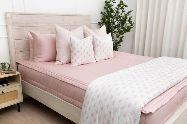 A bed made with pink zipper bedding and an assortment of light pink and floral pillows and blanket.