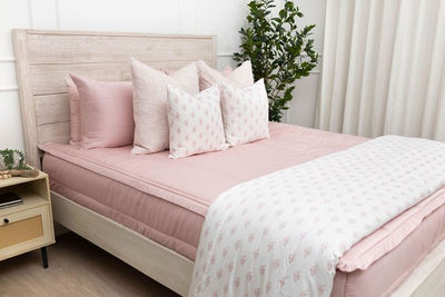 A bed made with pink zipper bedding and an assortment of light pink and floral pillows and blanket.