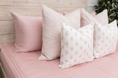 A close up view of a bed made with pink zipper bedding and an assortment of light pink and floral pillows.