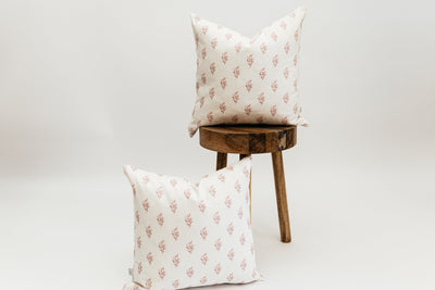 Two Ella pink floral pillows, one on a wooden stool and one leaning against the stool, both positioned in front of a white backdrop