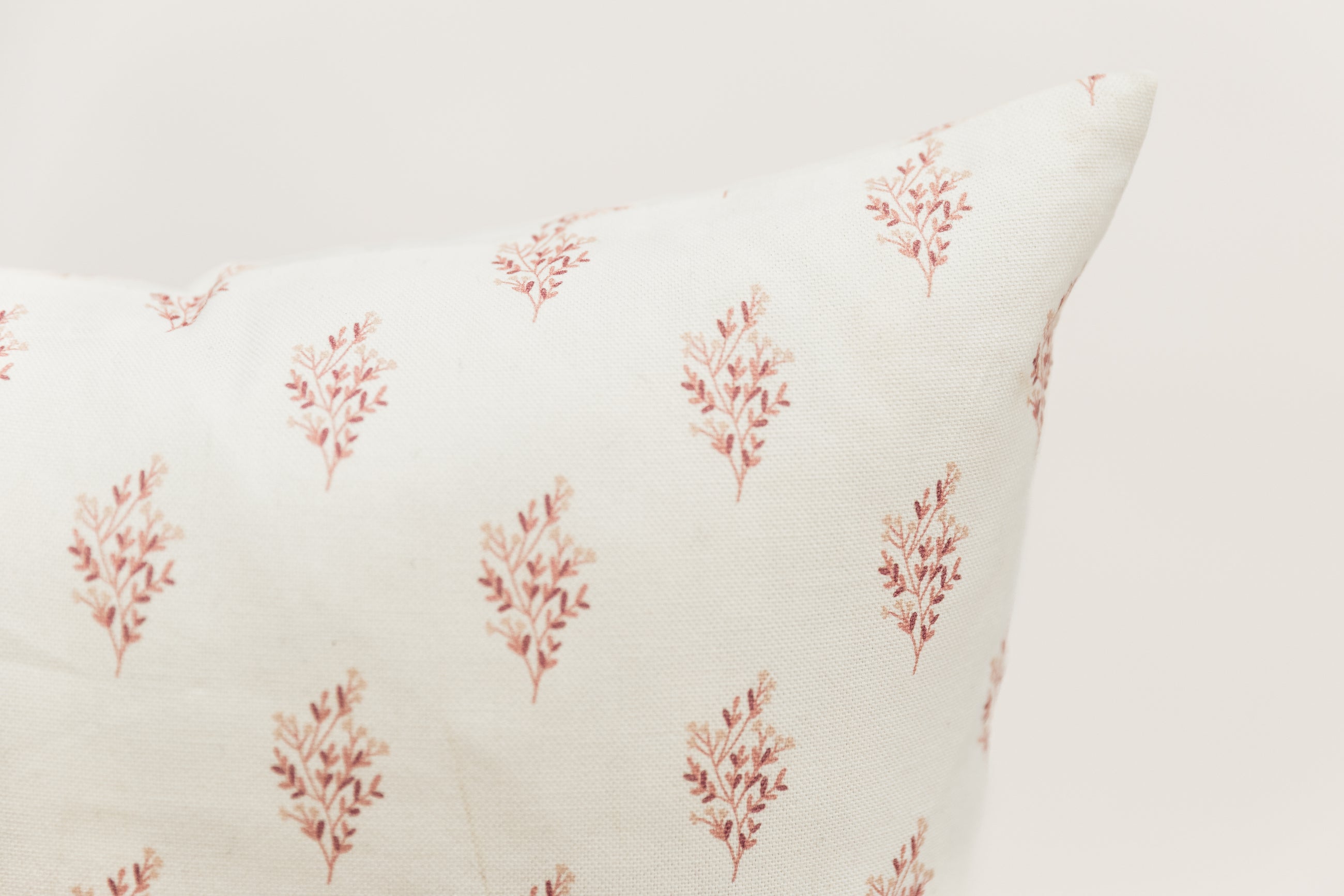 A close up of the floral detailing on a pink floral pillow positioned in front of a white backdrop.