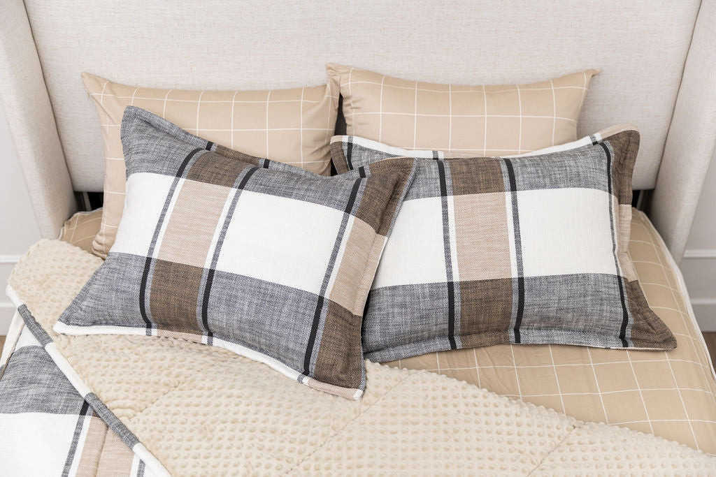 A bed made with cream, charcoal, and tan plaid zipper bedding with the comforter pulled back and pillows on top of the bed.