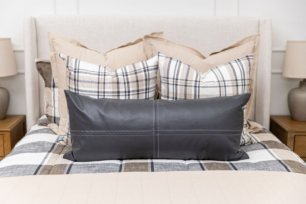 A close up view of a bed made with tan, cream, and charcoal zipper bedding and an assortment of neutral pillows and blanket.