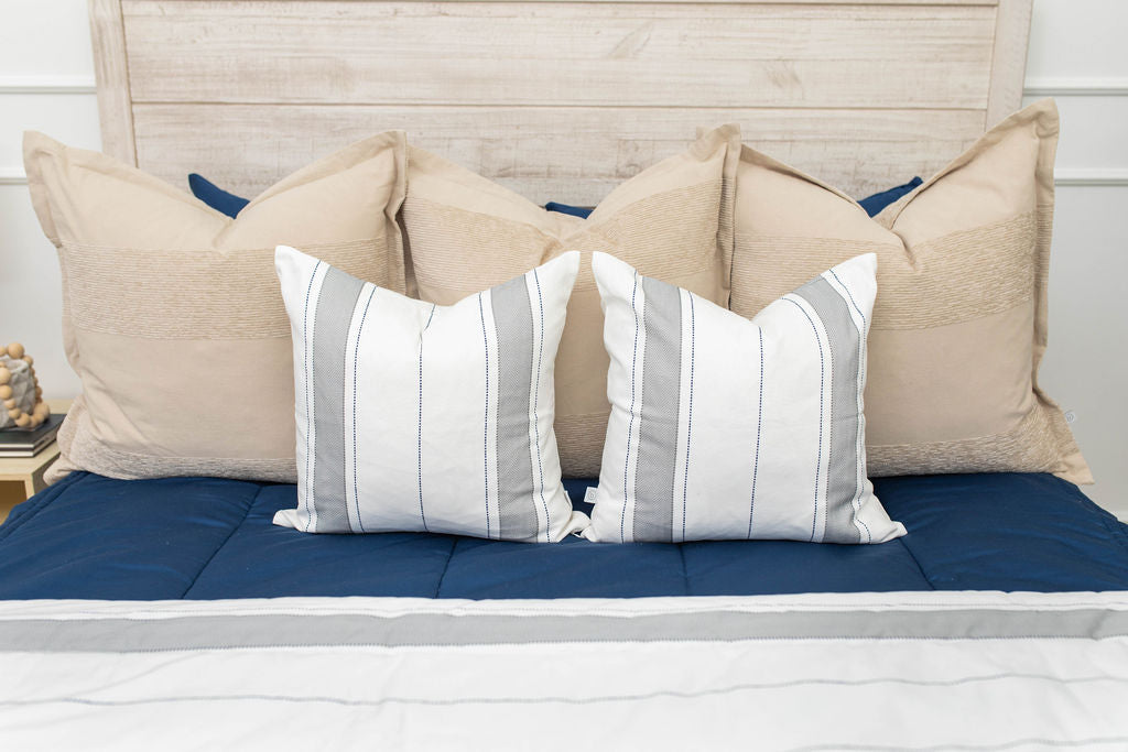 A close up view of a bed made with navy blue zipper bedding and an assortment of neutral and striped throw pillows and blanket.