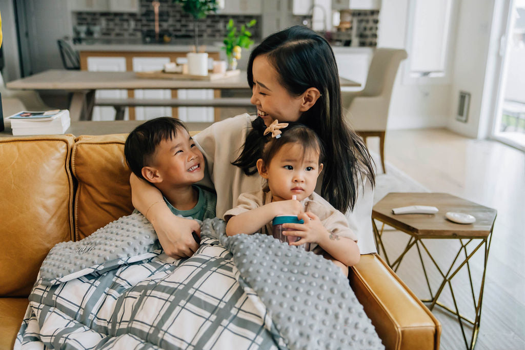 Mother and children laughing and cuddling on couch with a gray and white plaid children&