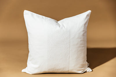 A white throw pillow on a brown backdrop.