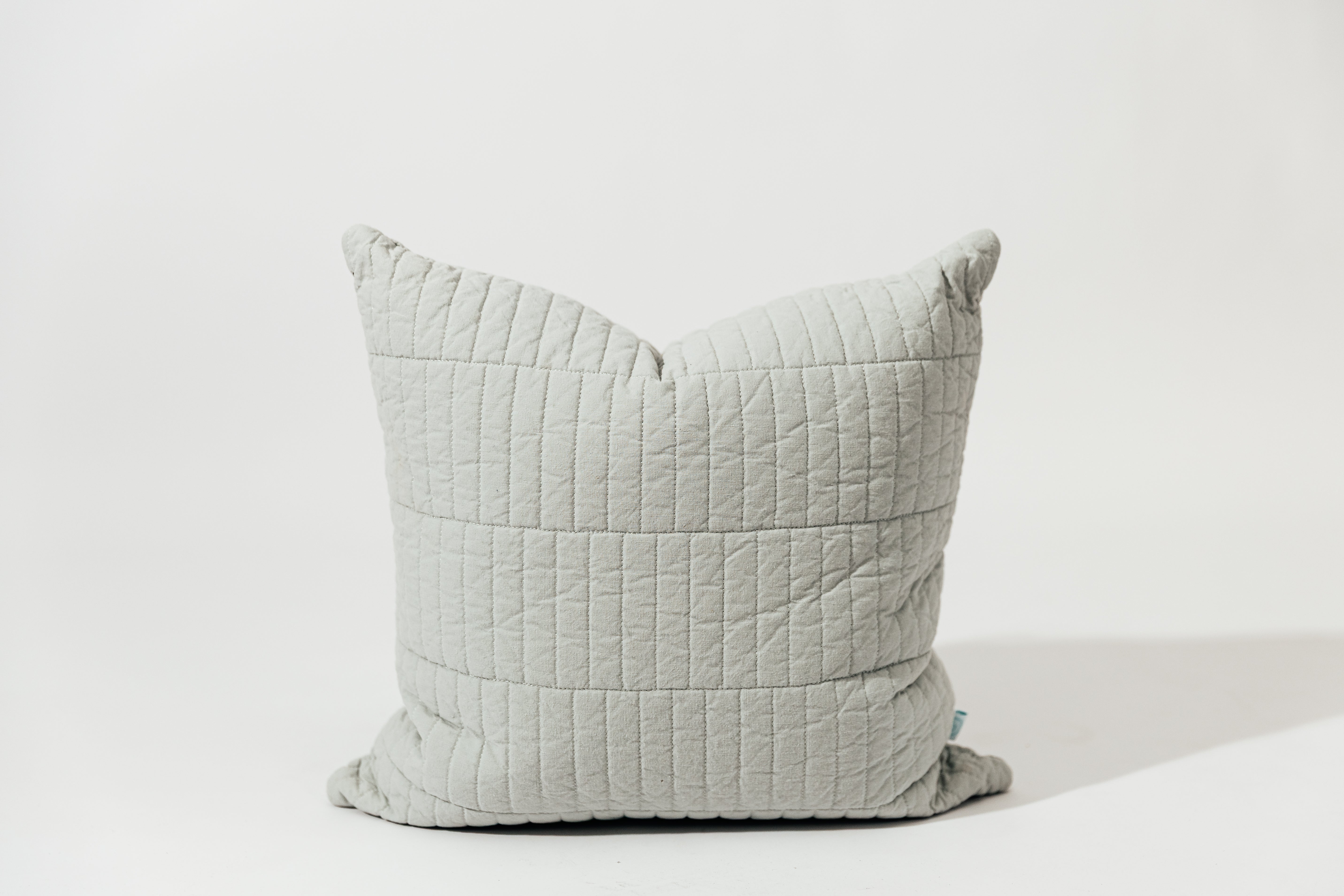 A blue pillow cover with piano tile quilted detail on a white backdrop.