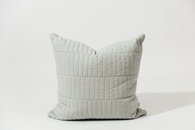 A blue pillow cover with piano tile quilted detail on a white backdrop.