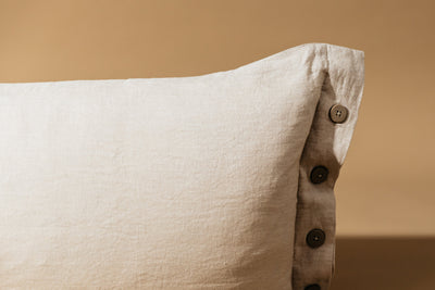 A close up on the button detailing of a lumbar linen pillow on a brown backdrop.
