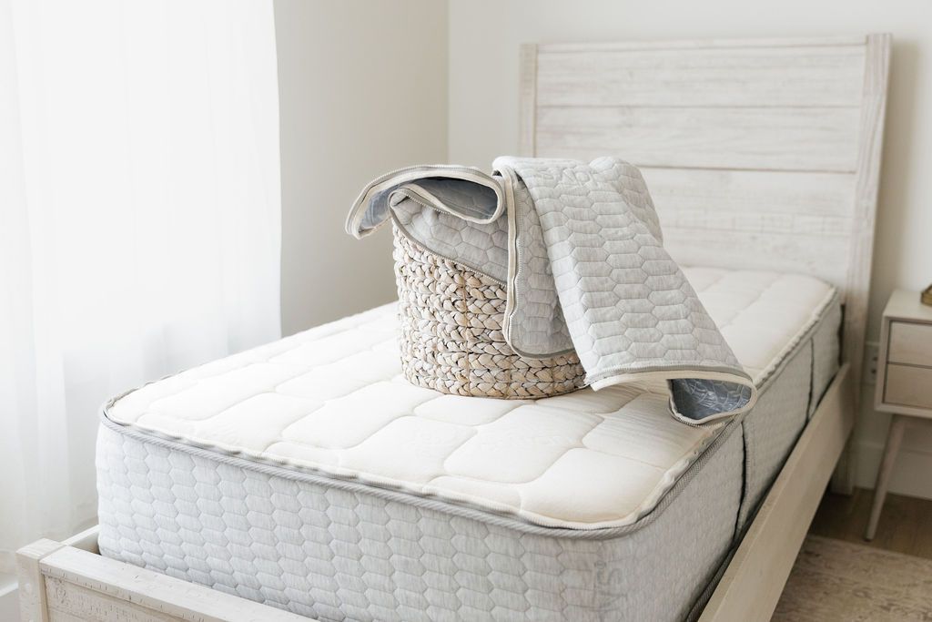 The removable, machine washable top of a zipper mattress sitting in a basket on top of the bed.