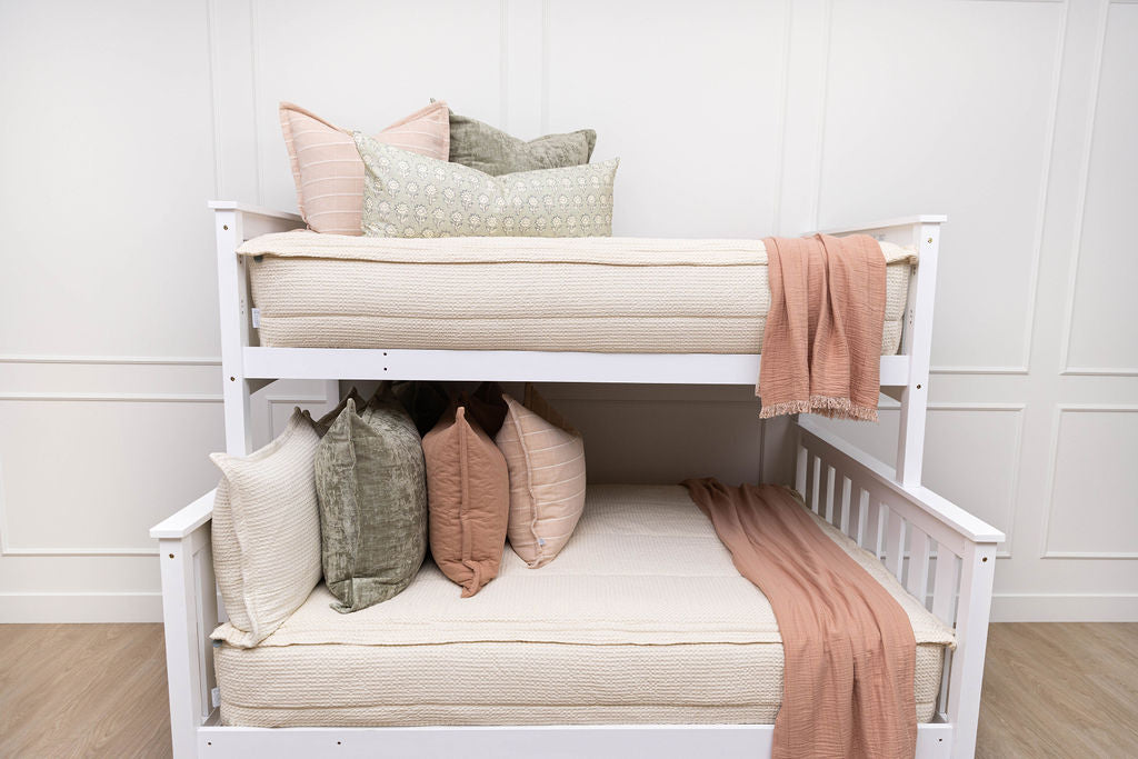 A standard bunk bed with both bunks made with cream waffle textured zipper bedding and neutral, green, and pink pillows and blankets.