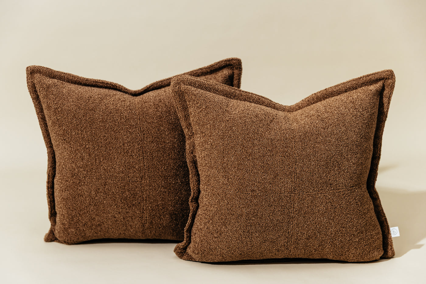 Two textured brown pillow covered arranged together on a cream backdrop.