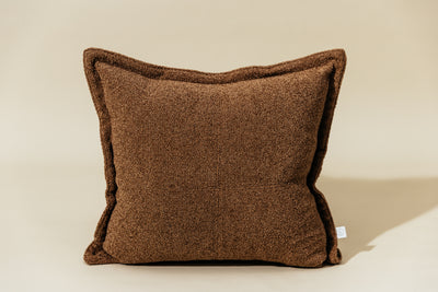 a textured brown pillow cover on a cream backdrop.