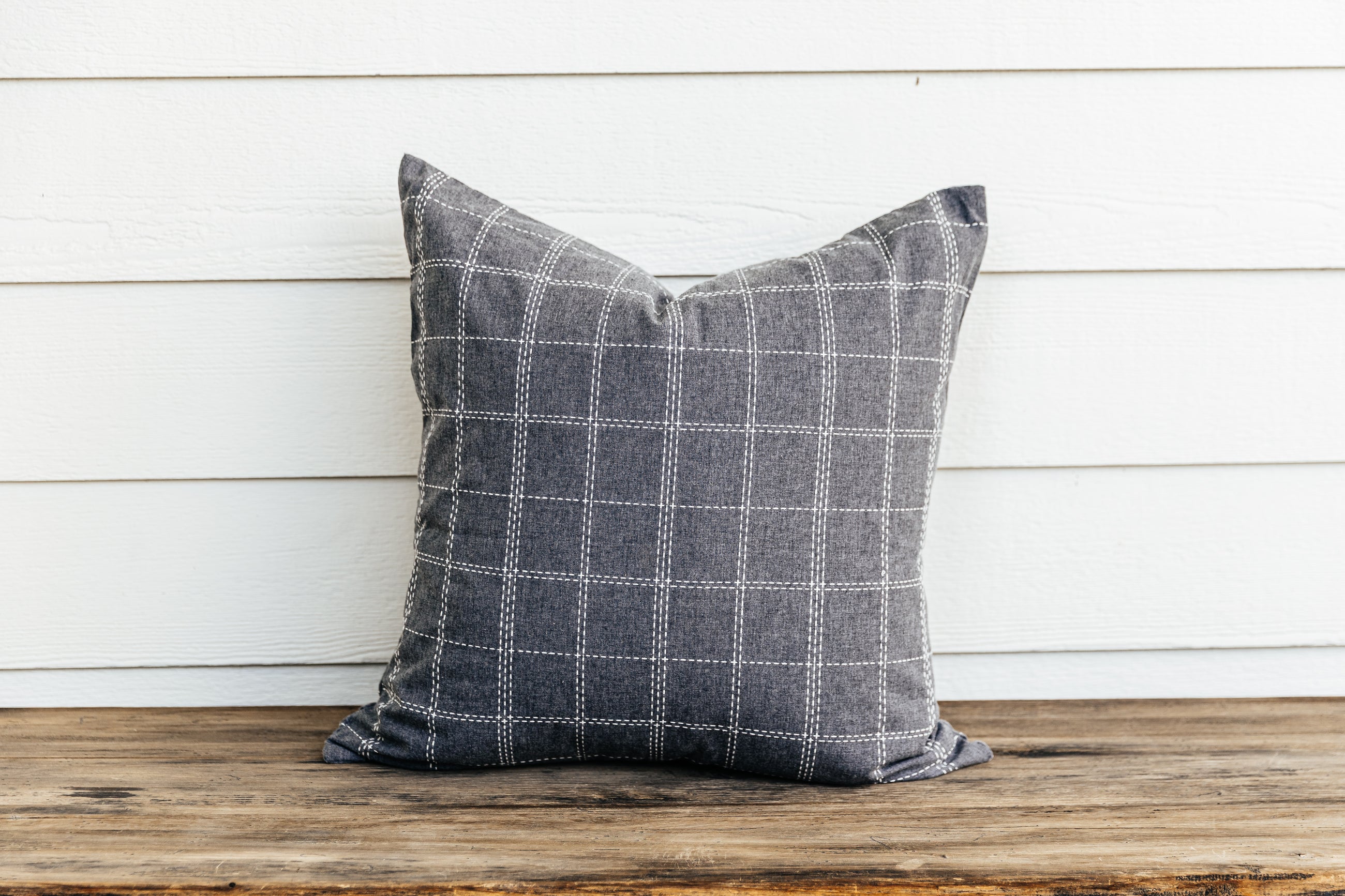 A grid pattern gray euro sham sitting on a wood bench with a white wood background.