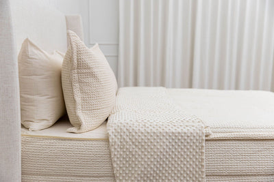 A side view of a bed made with cream waffle knit zipper bedding with the top unzipped and pulled back to show the inner minky lining.