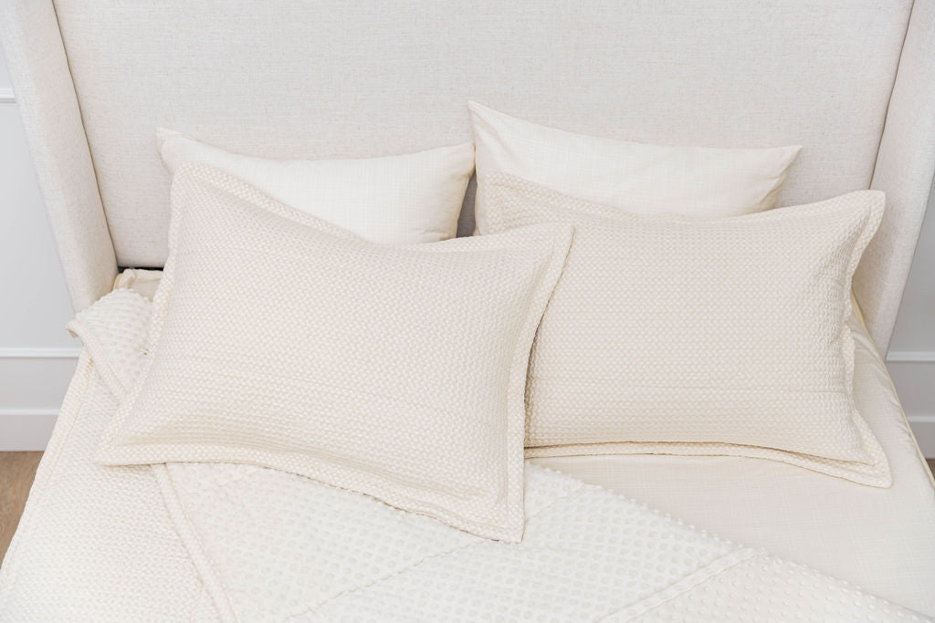 A bed made with cream waffle textured zipper bedding with the comforter pulled back showing minky interior lining and pillows on top of the bed.