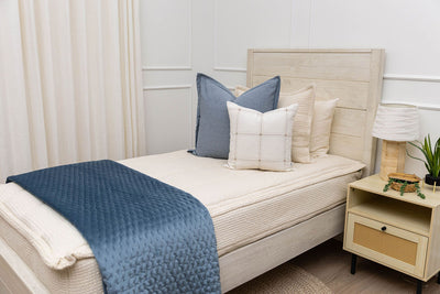 A twin bed made with cream waffle textured zipper bedding and an assortment of neutral and blue pillows and blanket.