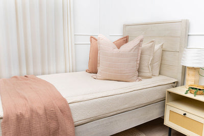 A twin bed made with cream waffle textured zipper bedding and an assortment of terracotta pillows and blanket.