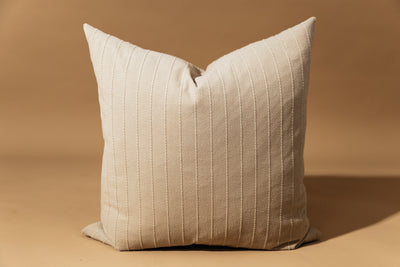 A neutral striped euro sham with vertical stitching arranged in front of a brown backdrop