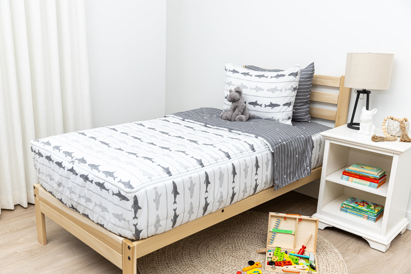 A twin bed made with shark kids zipper bedding, a nightstand next to it with books and toys strewn on the floor
