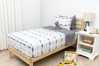 A twin bed made with shark kids zipper bedding, a nightstand next to it with books and toys strewn on the floor