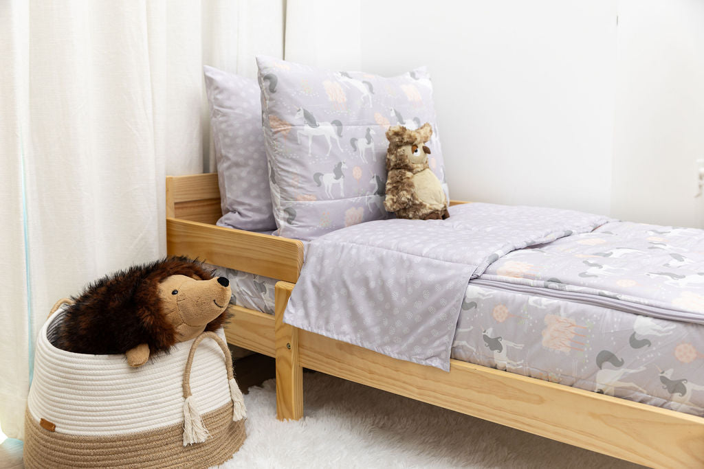 A toddler bed made with purple unicorn kids zipper bedding and a basket of stuffed animals beside it