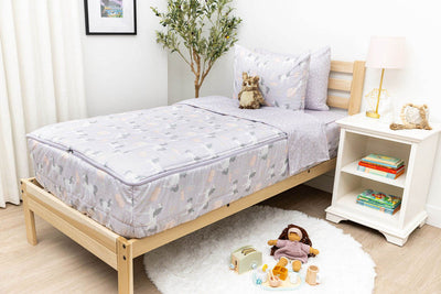 A twin bed made with purple unicorn kids zipper bedding, a nightstand beside it with books on the shelf and toys scattered on the floor