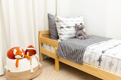 A toddler bed made with shark kids zipper bedding and a basket of stuffed animals next to it