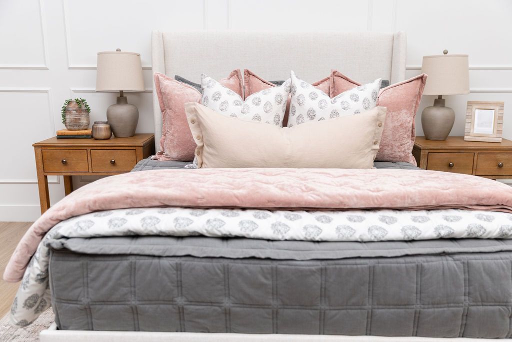 A bed made with gray zipper bedding and an assortment of floral and pink bedding accessories