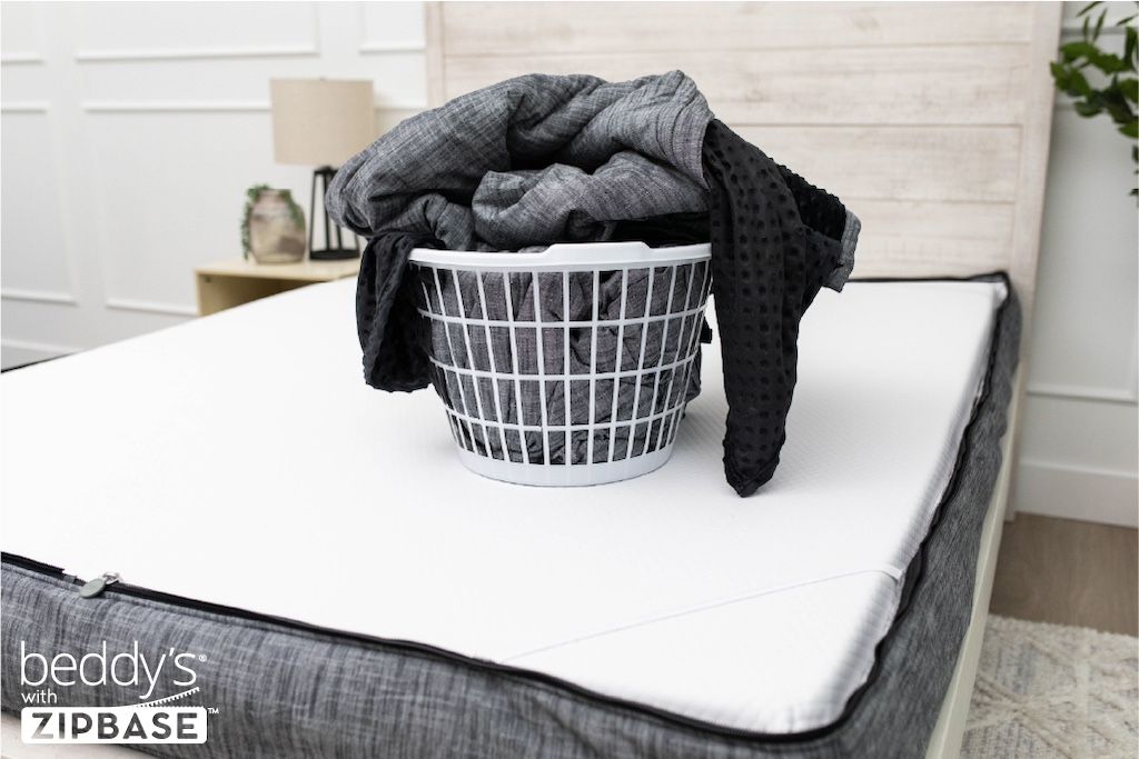 A bed made with just the fitted bedding base around the sides of the mattress, with the top comforter and ZipBase sheet in a basket on top of the bed.