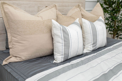 A close up view of a bed made with gray zipper bedding and an assortment of neutral and striped throw pillows and blanket.