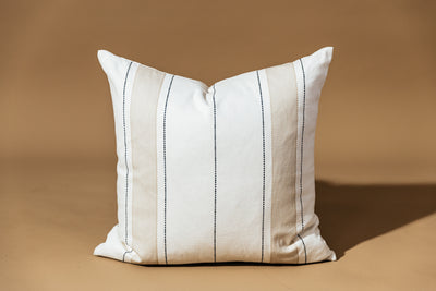 A white, tan, and black stripe pillow on a brown backdrop.