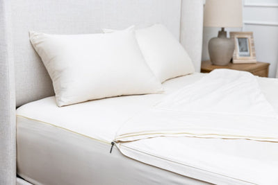 A side view of a bed made with white zipper sheets with the top sheet pulled back and pillows on top of the bed.