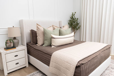 A queen bed made with brown zipper bedding and an assortment of cream and sage bedding accessories