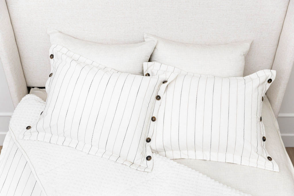 A bed made with white and textured pinstripes zipper bedding with the comforter pulled back and pillows on top of the bed.