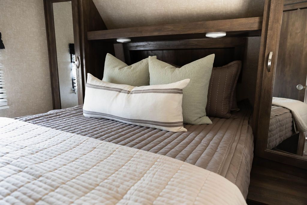 A queen bed in an RV made with brown zipper bedding and an assortment of neutral and sage bedding accessories