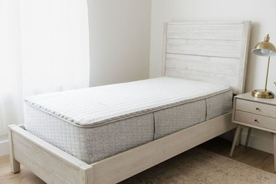 A zipper mattress on a twin bed frame next to a window in a bedroom.