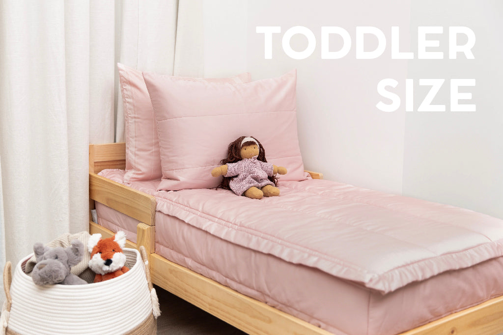 A toddler bed made with pink zipper bedding and a basket right next to the bed full of stuffed animals.