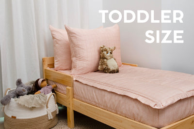 A toddler bed made with peach pink zipper bedding and a basket right next to the bed full of stuffed animals.