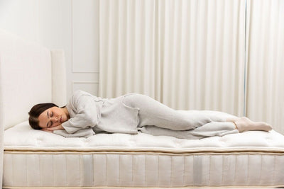 A woman in gray pajamas sleeping on top of a tufted mattress.