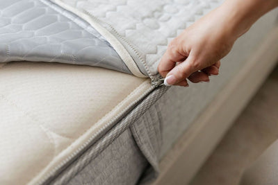 A woman pulling the zipper to remove the machine washable top of her zipper mattress.