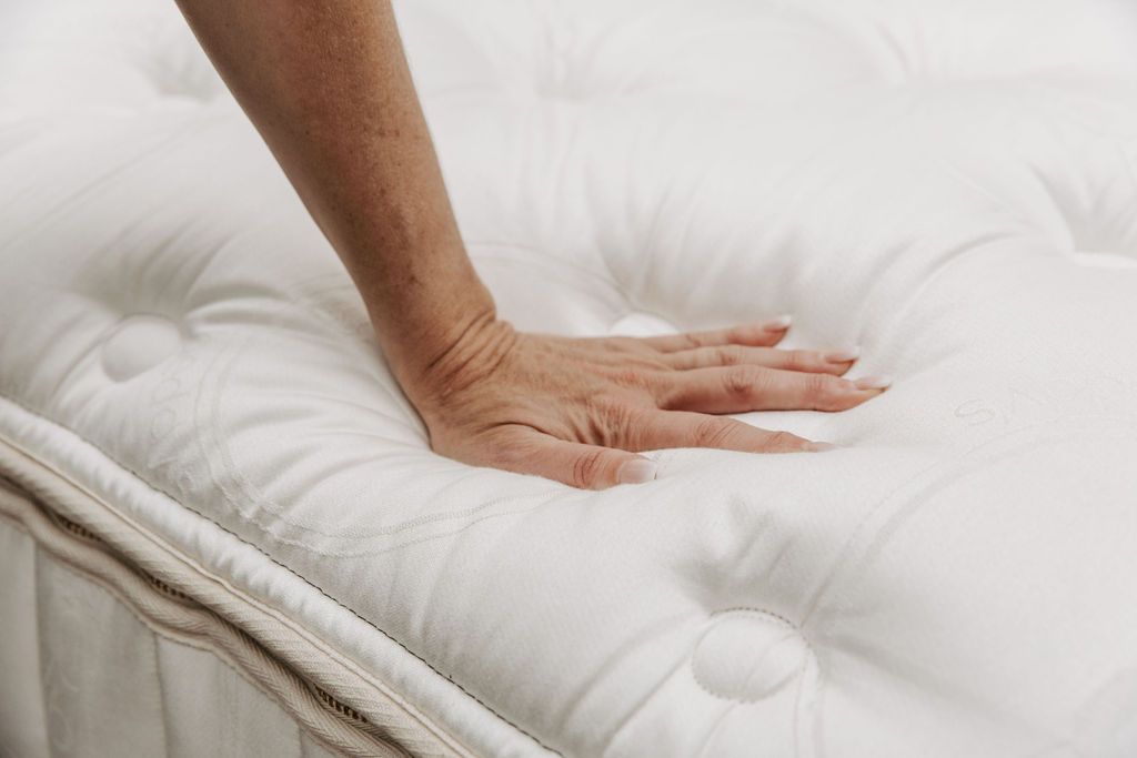 A hand pressing down on the top of the tufted mattress to show how padded and soft it is.