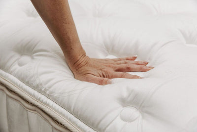 A hand pressing down on the top of the tufted mattress to show how padded and soft it is.