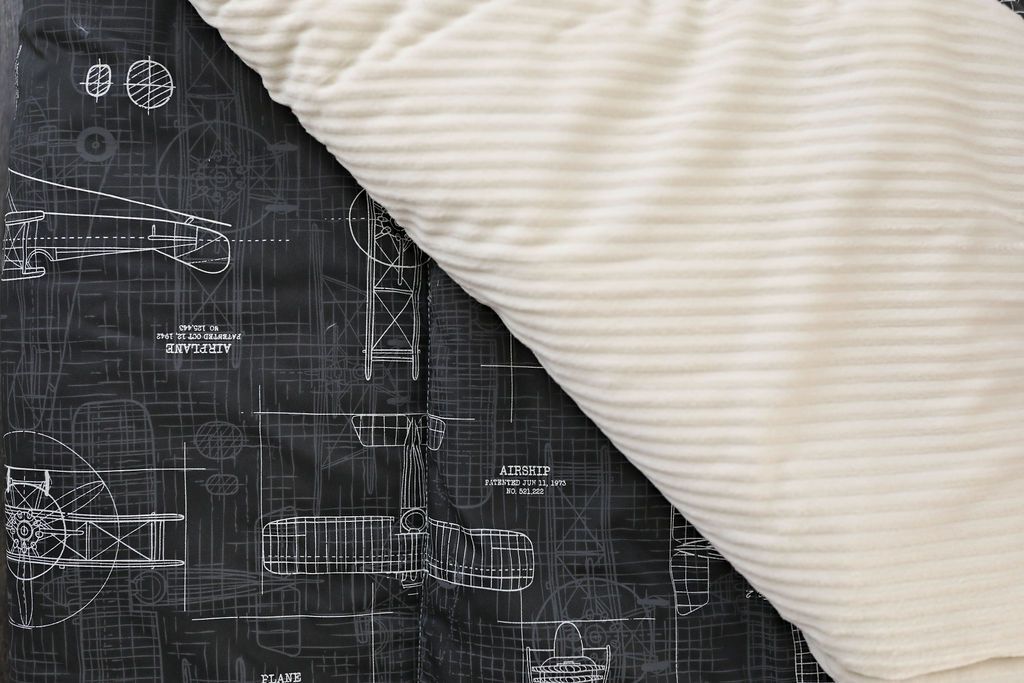 A charcoal airplane patterned blanket folded over to reveal the cream minky side.
