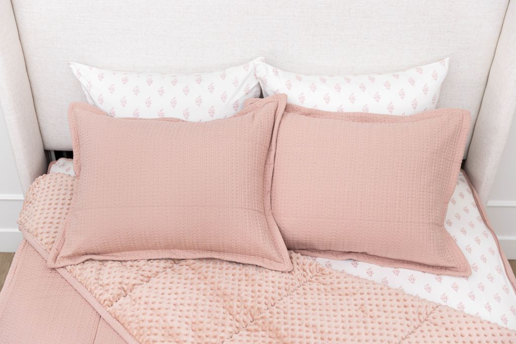 A bed made with woven pink zipper bedding with the comforter pulled back and pillows on top of the bed.