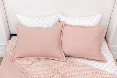 A bed made with woven pink zipper bedding with the comforter pulled back and pillows on top of the bed.