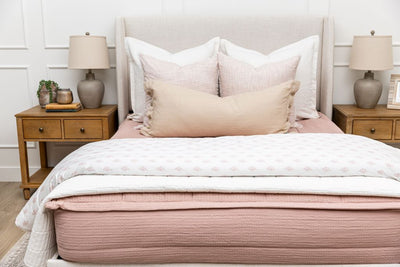 A bed made with woven pink zipper bedding and an assortment of neutral and pink pattern throw pillows and blankets.