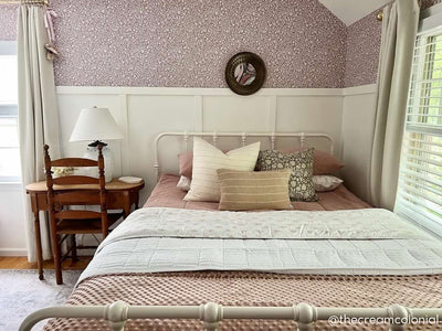 A bed made with woven pink zipper bedding and an assortment of neutral pillows and blankets.